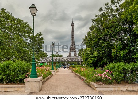 Urban park with green trees, flowers and lampposts as Eiffel Tower on background in Paris, France.