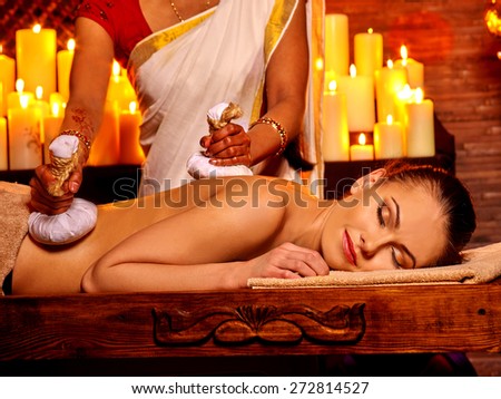 Woman having ayurvedic massage with pouch of rice. Burning candloe.