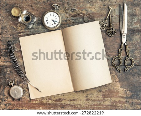 Still life with open book and antique writing tools on wooden background. Retro style toned picture