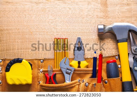 set of tools in toolbelt tape measure nippers djustable wrench pliers pencil hammer cutter on wooden board  Royalty-Free Stock Photo #272823050