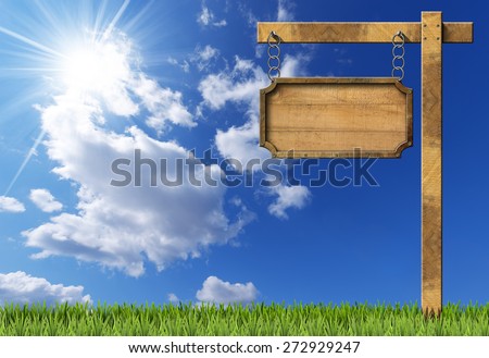Wood and Metal Sign with Chain and Pole. Empty rectangular wooden sign with metallic brown frame hanging with metal chain on a wooden pole, on blue sky with clouds, sun rays and green grass