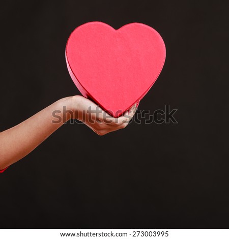 Valentines day, love, romance concept. Woman hand holding heart shaped gift box on dark gray background.
