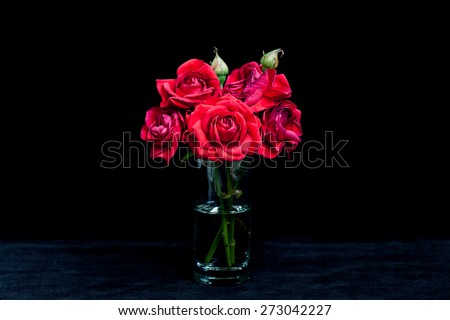 Floral background, wallpaper, greeting card image. Bouquet of red roses in glass vase on  black velvet texture.
