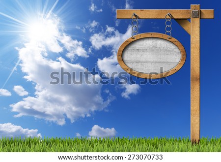 Oval Sign with Frame Chain and Pole. Empty oval wooden sign with wooden brown frame hanging with metal chain on a wooden pole, on blue sky with clouds, sun rays and green grass