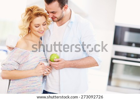 A picture of a young couple eating breakfast and hugginh in the kitchen