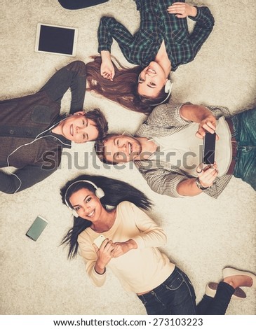 Happy multiracial friends relaxing on a carpet with gadgets 