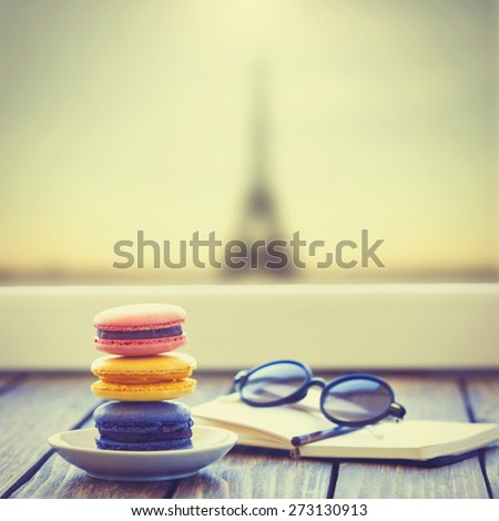 Macarons and little notebook with glasses on wooden table and Eiffel tower background