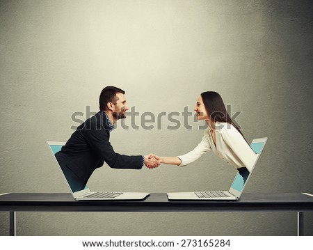 smiley businessman and businesswoman come out from laptop, shaking hands and looking at each other over dark grey background Royalty-Free Stock Photo #273165284