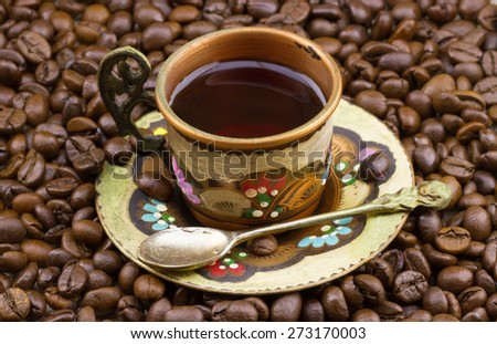 Traditional painted copper cup of coffee with heap of roasted coffee beans