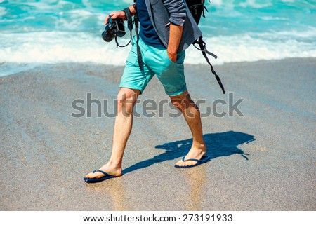 Man in shorts walking with photo camera on the beach