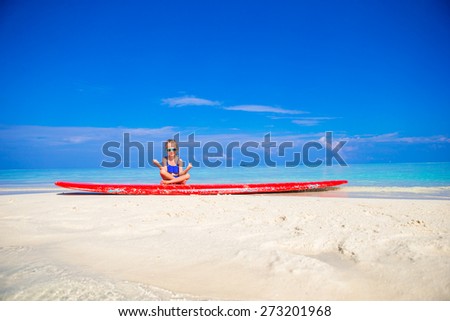 Little girl in yoga position meditating on surfboard