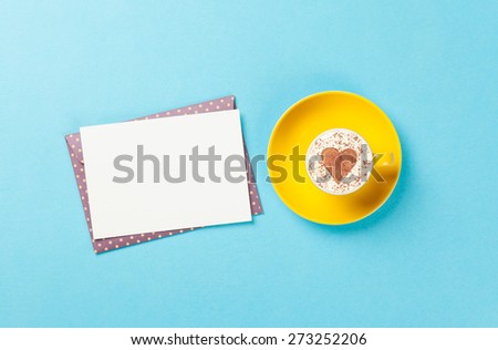 Cup of cappuccino with heart shape and envelope on blue background.