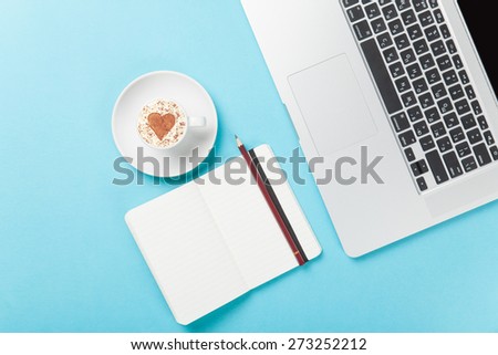 Cup of cappuccino with heart shape and laptop with note on blue background.