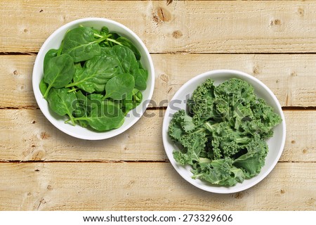 Two white bowls one containing spinach leaves and one containing chopped kale leaves. Shot from above on a rustic wooden background Royalty-Free Stock Photo #273329606