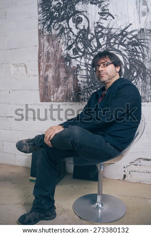 Portrait of painter artist posing in front of one modern artwork in his studio