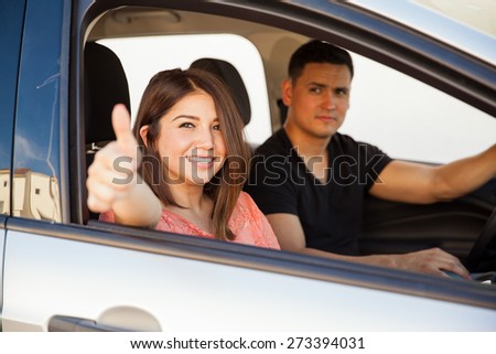 Pretty young brunette with a thumb up as sign of approval for the car they are driving