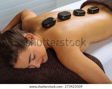 Photo of a young woman lying in a spa having a hot stone treatment. Focus on the first two stones.