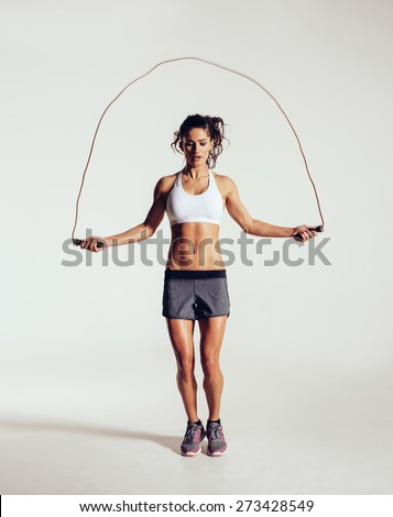 Fit young woman skipping rope. Portrait of muscular young woman exercising with jumping rope on grey white background. Royalty-Free Stock Photo #273428549