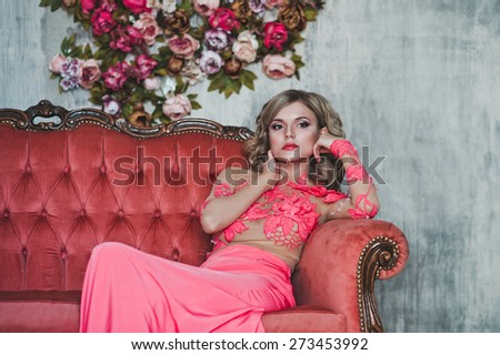 The girl in a pink dress sits on a sofa.