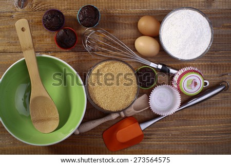 Ingredients and appliances for makeing cupcakes such as brown cane sugar flour and eggs on the wooden table, horizontal picture