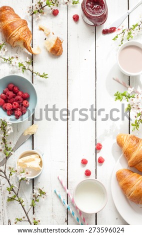 Romantic french or rural breakfast - cocoa, milk, croissants, jam, butter and raspberries on rustic white wood table from above. Countryside weekend morning concept. Background with free text space. Royalty-Free Stock Photo #273596024