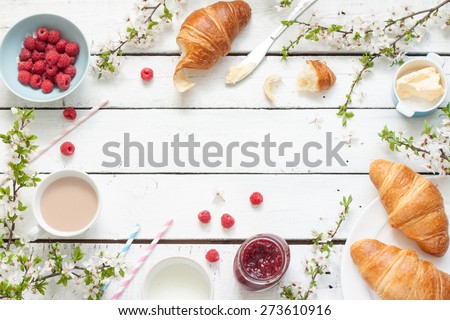 Romantic french or rural breakfast - cocoa, milk, croissants, jam, butter and raspberries on rustic white wood table from above. Countryside weekend morning concept. Background with free text space. Royalty-Free Stock Photo #273610916