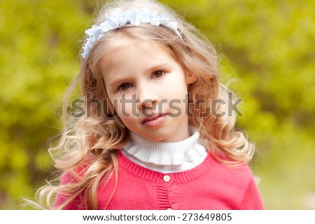 Beautiful child 4-5 year old girl posing over green nature background. Looking at camera. Wearing floral hairband. 