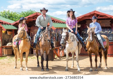 happy cowboy family of four on horsebacks waving their hands
