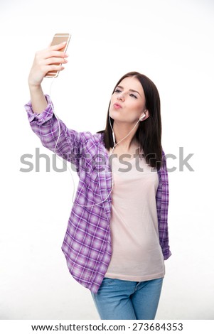 Young woman in headphones making selfie photo on smartphone over white background
