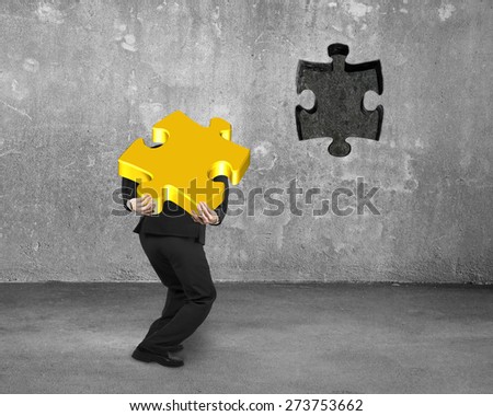 Businessman carrying 3D gold jigsaw puzzle piece to insert the dark hole on concrete wall background