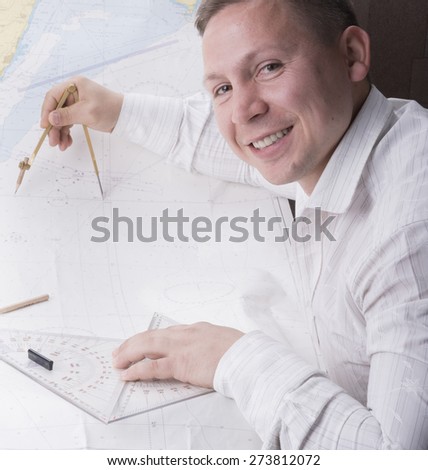 young smiling navigator is measuring with divider on navigation map

