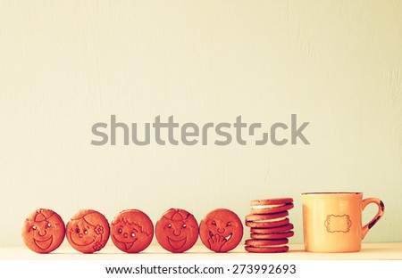 raw of cookies with smiley face over wooden table next to cup of coffee. image is retro style filtered
