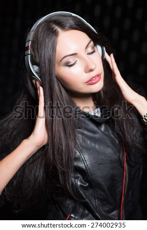 Portrait of pretty brunette posing with headphones and closed eyes. Isolated on black
