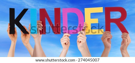 Many Caucasian People And Hands Holding Colorful Straight Letters Or Characters Building The German Word Kinder Which Means Kids On Blue Sky