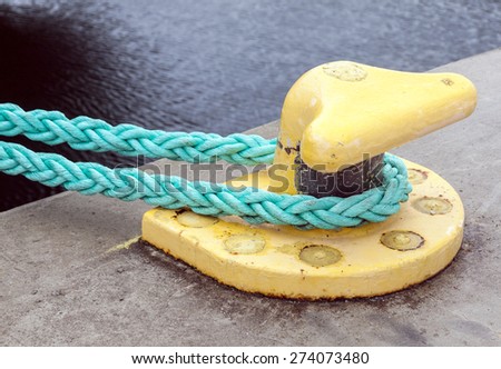 Horizontally oriented picture of port pier with yellow mooring bollard and green ropes