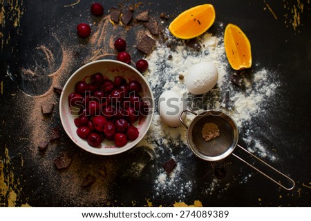 Muffin ingredients: the frozen cherry in a plate, orange segments, eggs, flour on a dark wooden background