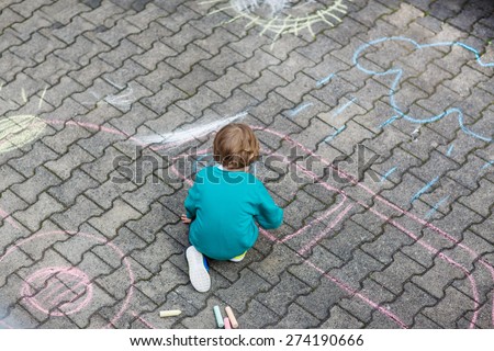 Funny  little child painting car with colorful chalks outdoors in summer. Kid having fun. Creative leisure with children outdoors.