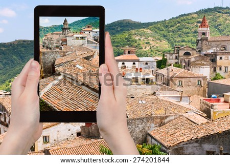 travel concept - tourist takes picture of ancient tile roofs and tower of Sant Antonio church in Castiglione di Sicilia on tablet pc