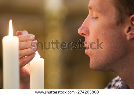 Closeup of man protecting candle flame in church