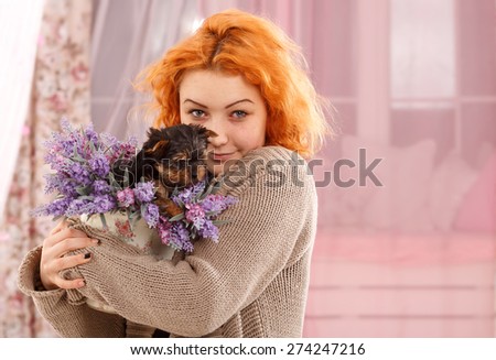 Young girl with a puppy Yorkshire terrier. Beautiful young woman holding a vase with a flower in her hand. Flower pots sitting small puppy York terrier . Woman and puppy dog in a pink interior room. 