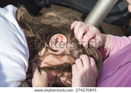Mother looking for head lice at her little daughter to sunlight