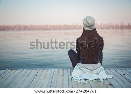 Girl sitting on pier and lookingat the river Royalty-Free Stock Photo #274284761