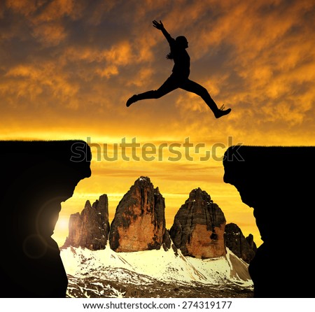 Silhouette the girl jumping over the gap at sunset in the background  Tre Cime di Lavaredo, Dolomite Alps, Italy