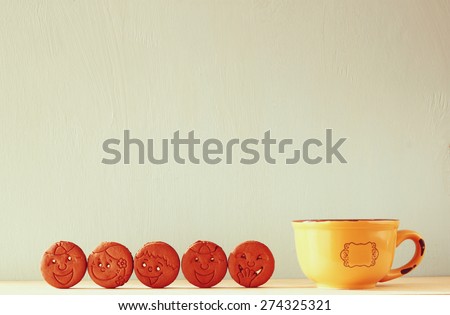 raw of cookies with smiley face over wooden table next to cup of coffee. image is retro style filtered 