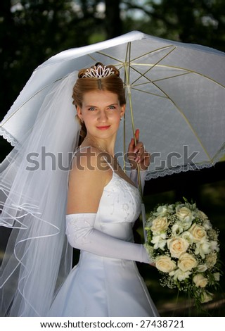 Portrait of pretty bride pictured in traditional white wedding dress. She is holding a bouquet and parasol, and is looking happy.