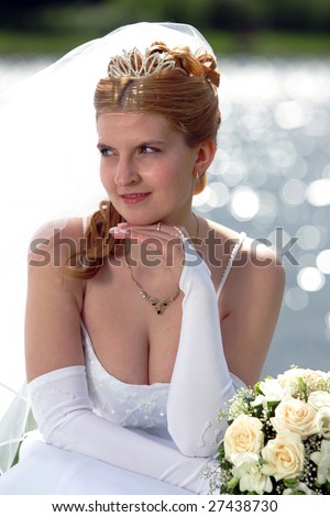 Portrait of pretty bride pictured in traditional white wedding dress. She is holding a bouquet and wearing a veil.