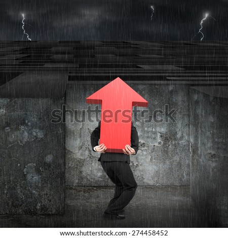 Man carrying big 3D red arrow up sign entering the huge maze with dark night heavy rain background