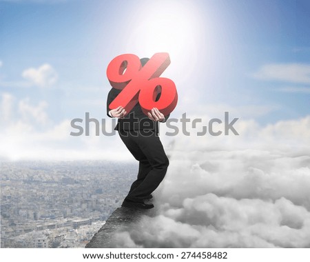 Man carrying big 3D red percentage sign balancing on concrete ridge with sky cloudscape cityscape sunlight background