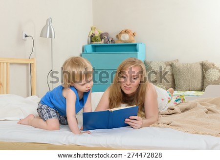 woman shows a child reading a book lying on the bed