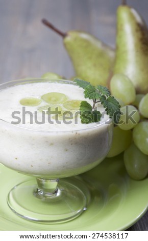  Smoothies of pears and green grapes with yogurt in a glass bowl. Pears and grapes lying on a table nearby.
 